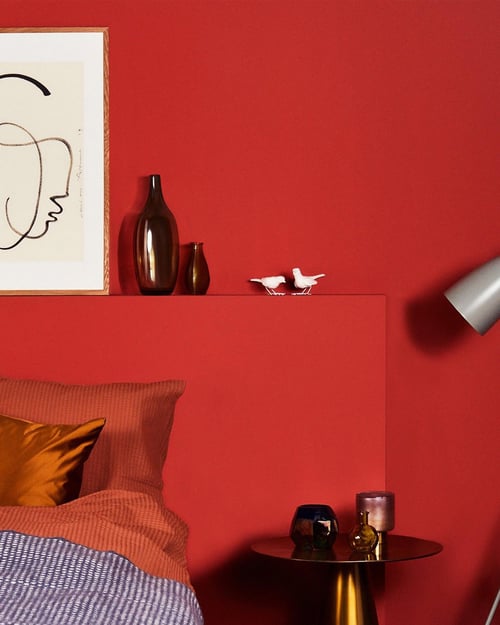 Rode slaapkamer met oranje gekleurd beddengoed en sierkussen