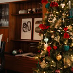 Woonkamer met rijkelijk gevulde kerstboom met kerstornamenten van de Bijenkorf home en Vondels