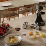 tafel met een glas rode wijn met pasta elementenset van KitchenAid en een mat zwarte KitchenAid keukenmachine