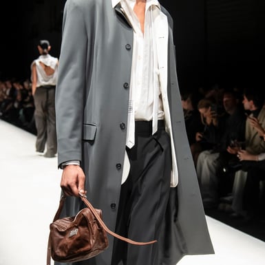 Model op de catwalk in een grijze trenchcoat