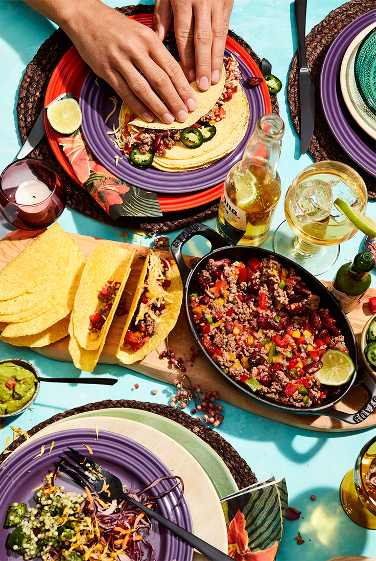 Vrolijk gekleurd servies in aubergine paars en rood met tacos en tacovulling in een hapjespan