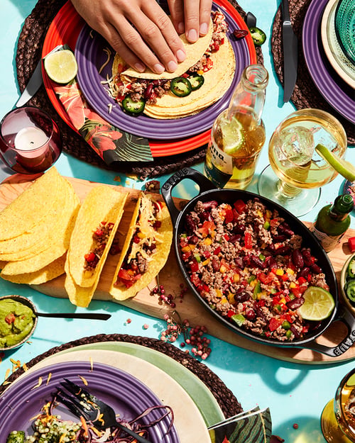 Vrolijk gekleurd servies in aubergine paars en rood met tacos en tacovulling in een hapjespan